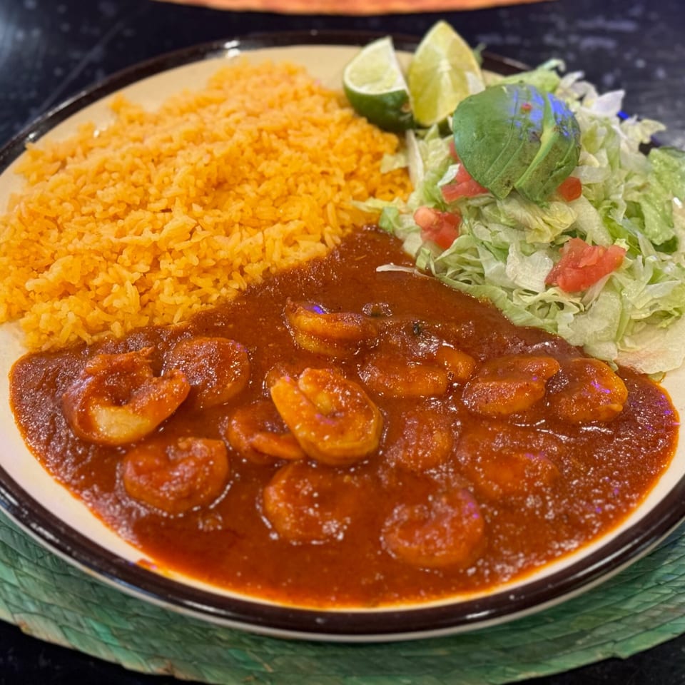 Shrimp in red sauce with orange rice, shredded lettuce, diced tomatoes, and lime wedges.