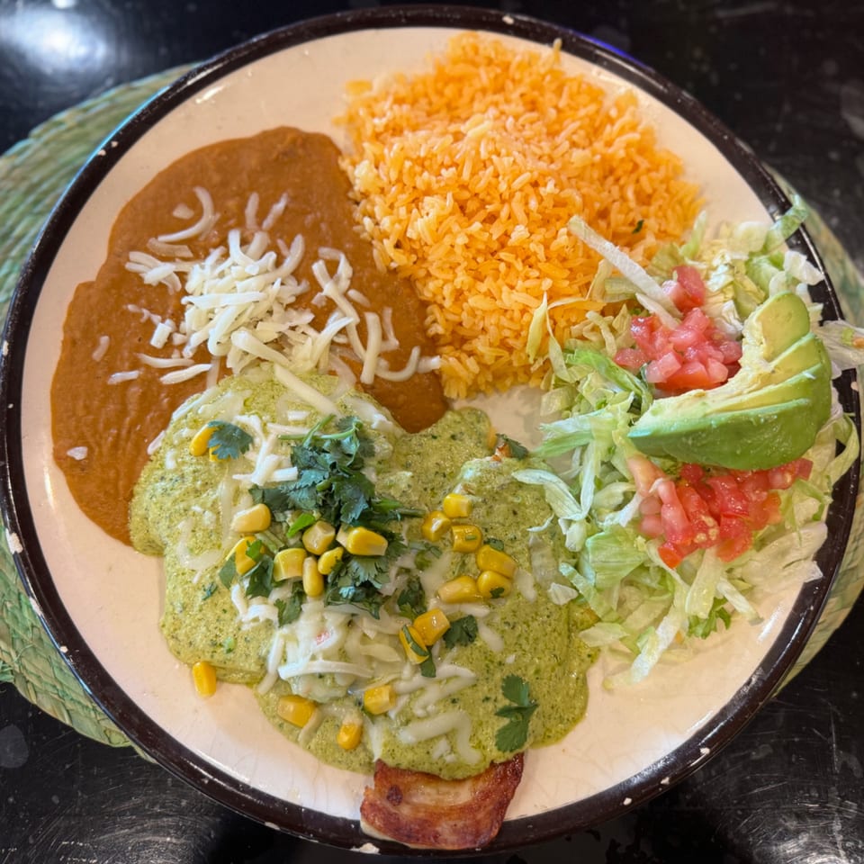 A Mexican dish with green enchiladas, refried beans, rice, and a side salad with avocado.