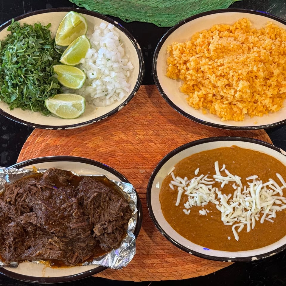 Four bowls of Mexican food: shredded beef, rice, refried beans with cheese, and cilantro with onions and limes.