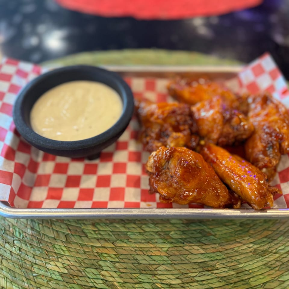Sweet and spicy chicken wings with a side of ranch dressing on a red and white checkered paper.