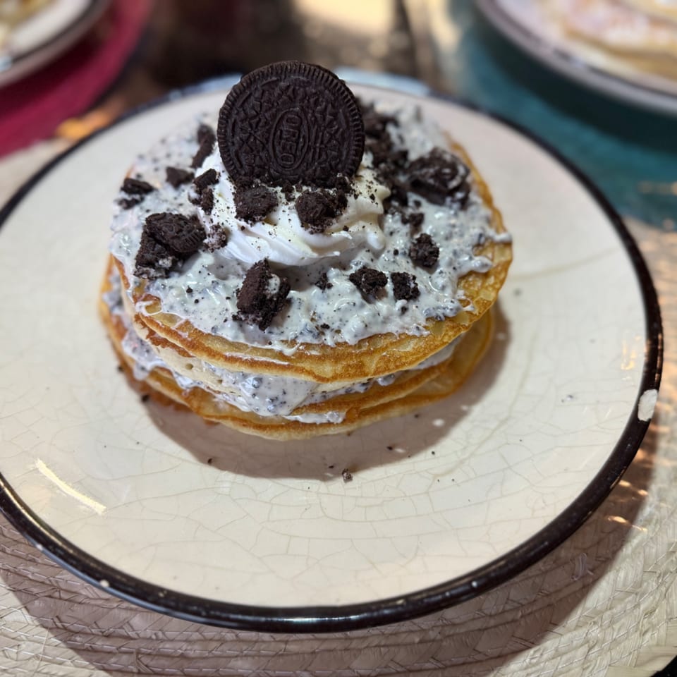 Stack of pancakes topped with cookies and cream frosting, crumbled cookies, and an Oreo.