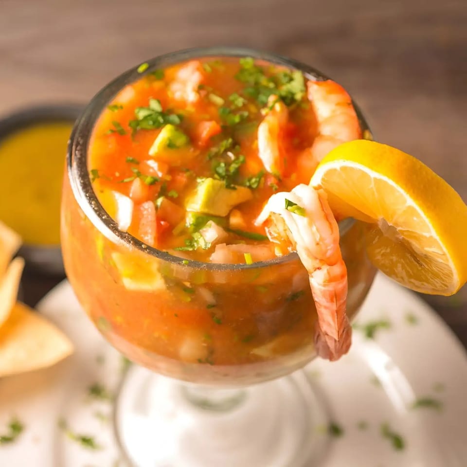Mexican shrimp cocktail with avocado, cilantro, and a lemon wedge in a glass.