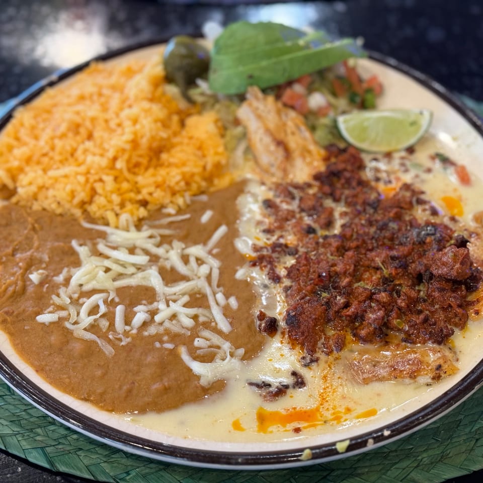 A Mexican dish with rice, refried beans, and a meat and cheese entree, garnished with lime and avocado.