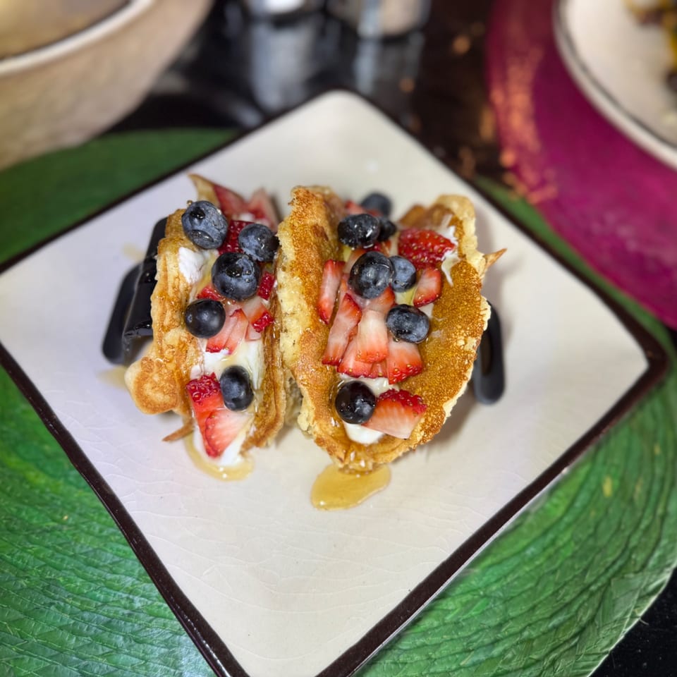 Two waffle tacos filled with whipped cream, blueberries, strawberries, and drizzled with honey.