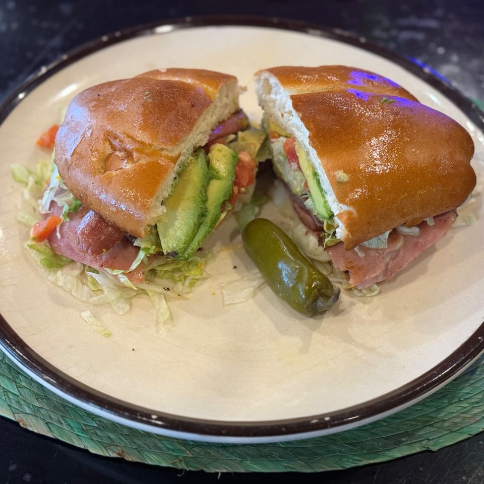 A Mexican torta sandwich, cut in half, with avocado, lettuce, tomato, and a jalapeño.