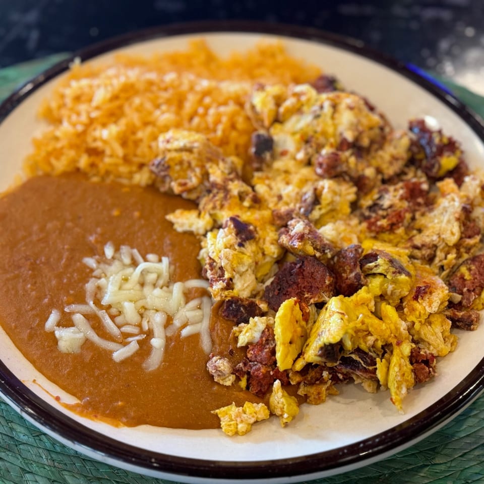 Scrambled eggs with chorizo, refried beans topped with cheese, and a side of orange rice.