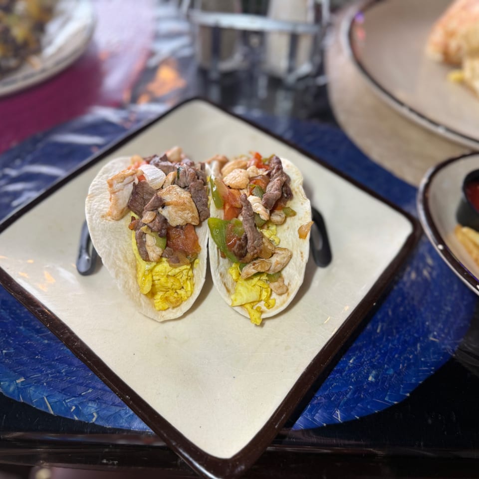 Two breakfast tacos filled with scrambled eggs, steak, chicken, shrimp, and vegetables on a plate.