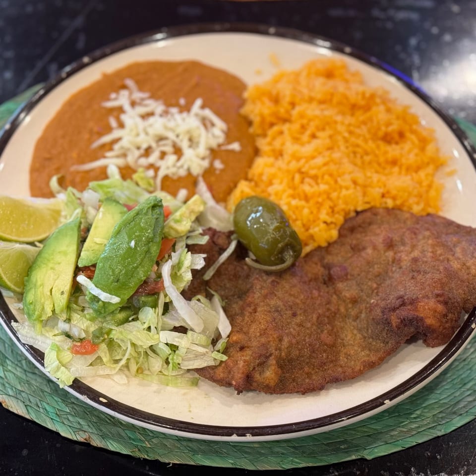 A plate of Mexican food with fried meat, rice, refried beans, salad, and a jalapeño.