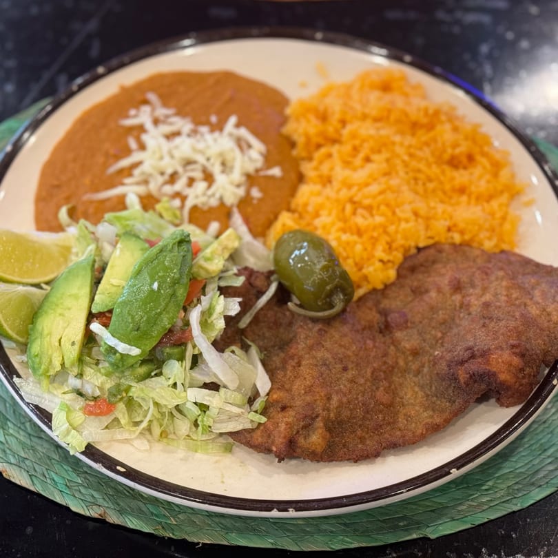 A plate of Mexican food with fried meat, rice, refried beans, salad, and a jalapeño.