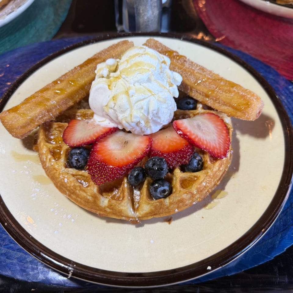 Waffle topped with ice cream, strawberries, blueberries, and two churros drizzled with syrup.